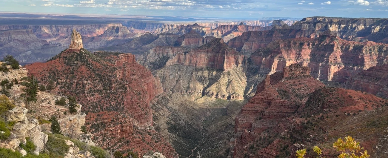 Panoramic view of a canyon with rugged terrain and colorful rock formations under a cloudy sky